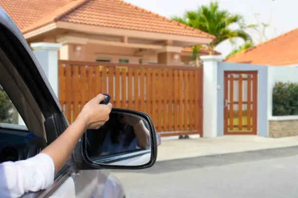 Woman in car,hand holding and using remote control to open the automatic door with modern home blurred background. Auto gate or garage, electric door concept.
