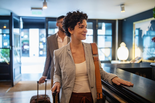 Business travelers arriving at hotel reception desk. Young businesswoman with male colleague walking in the hotel.