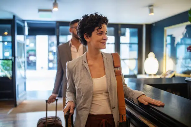 Business travelers arriving at hotel reception desk. Young businesswoman with male colleague walking in the hotel.