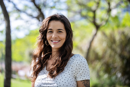 Portrait of a mid adult woman standing at the park. Attractive female in casuals looking at camera and smiling.