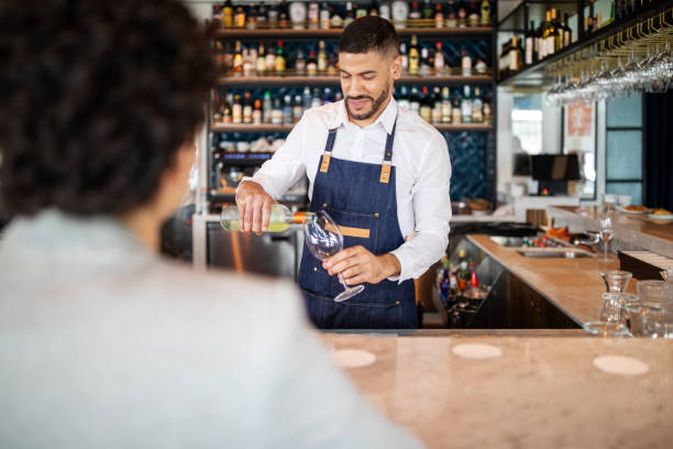 Bartender serving wine to a woman Barman pouring wine into a glass with a woman sitting at bar counter. Bartender serving wine to a woman in bar. cocktail bar busy stock pictures, royalty-free photos & images