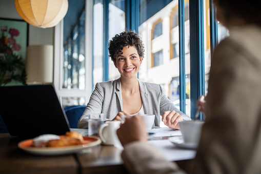 Young businesswoman having brunch with female colleague at cafe. Two business women talking while having a coffee at restaurant.