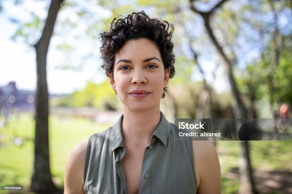 Portrait of a confident young woman at the park Portrait of a confident young woman standing at the park. Beautiful female in casuals looking at camera. Women Stock Photo