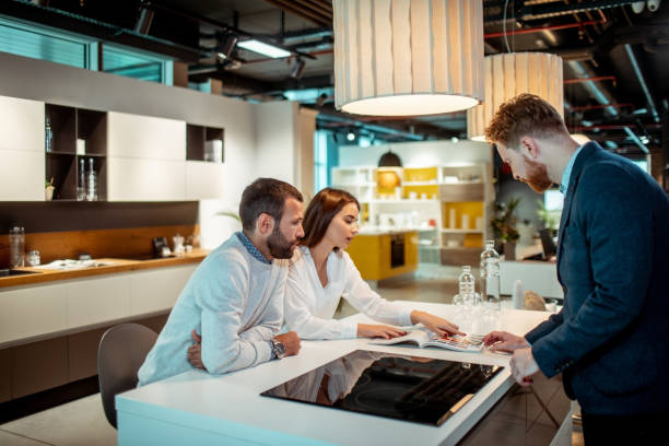 istock Young wife looking at a catalog while shopping for kitchen appliances with her husband with the help of a store clerk in a kitchen equipment shop 1191198625