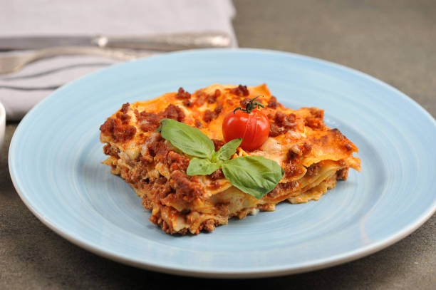 istock Serving of lasagna on a light plate.  Lasagna garnished with cherry tomatoes and fresh basil leaves. 1191198989