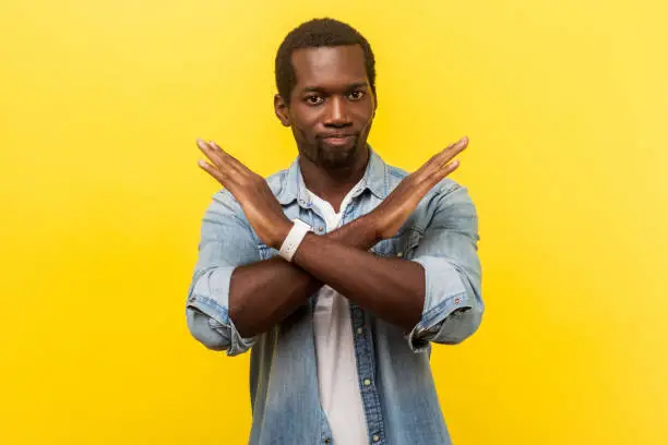 Photo of Never again. Portrait of absolutely convinced man crossing hands, showing x sign. indoor studio shot isolated on yellow background