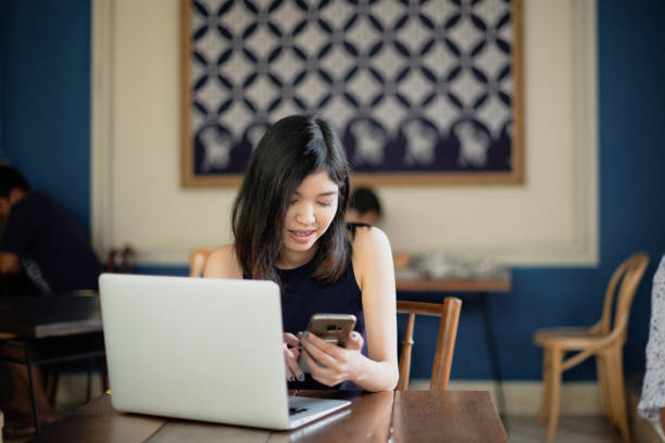 istock Asian girl freelance using smartphone while working with her laptop in coffeeshop. 1191202798