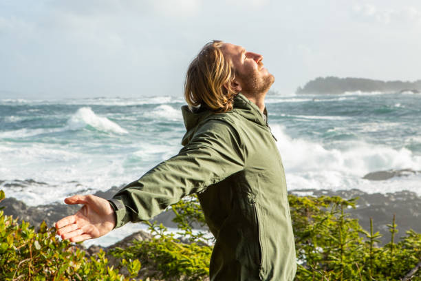 istock Young man standing on coastline arms outstretched, wilderness area 1191206302
