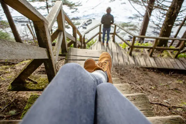 Personal perspective of woman sitting on wooden stairs and young man watching the sea from woodland, Tofino, Canada