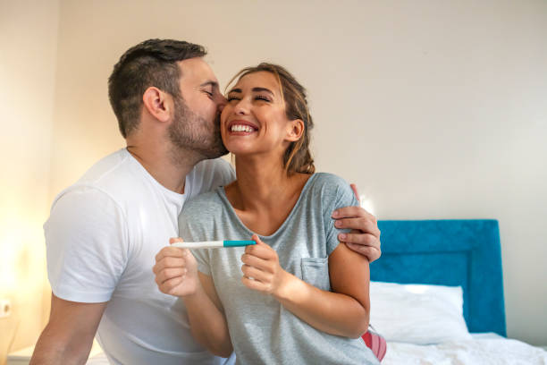 Young couple is happy because of positive pregnancy test. Young couple is happy because of positive pregnancy test. Affectionate couple finding out results of a pregnancy test in their bedroom. Family, parenting and medical concept pregnancy test stock pictures, royalty-free photos & images