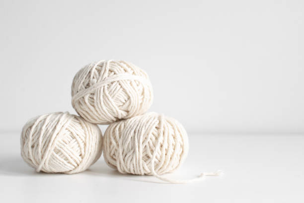 Balls of white yarn on a white wall background. Threads of wool boho image. Space for text. Good for macrame and handicrafts banners and advertisement stock photo