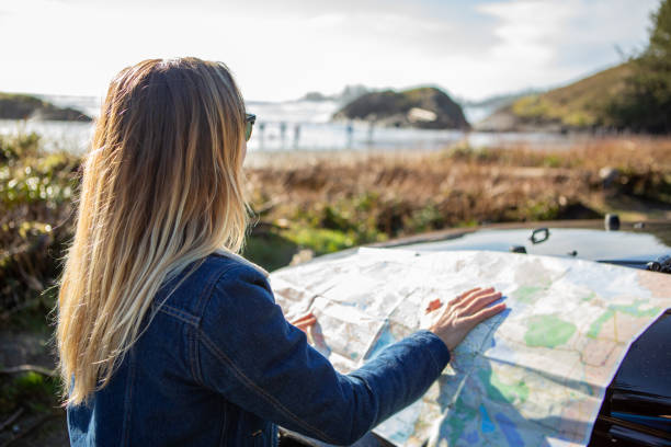 Young woman standing near 4x4 by the beach looking at road map Young woman standing near 4x4 by the beach looking at road map canada road map stock pictures, royalty-free photos & images