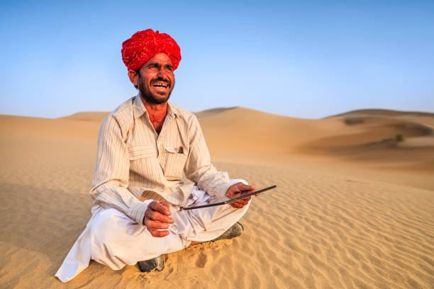 Indian man using a digital tablet on sand dunes, desert village, Rajasthan, India.