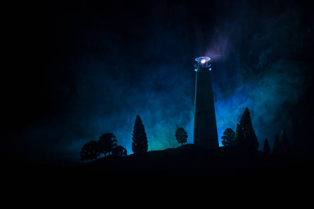 istock Lighthouse with light beam at night with fog. Old lighthouse standing on mountain. Table decoration. Toned background. Moonlighting. 1191214802