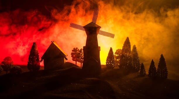 Windmill silhouette standing on hill against the night sky. Night decor with old windmill on hill with horror toned foggy background with light. Horror concept