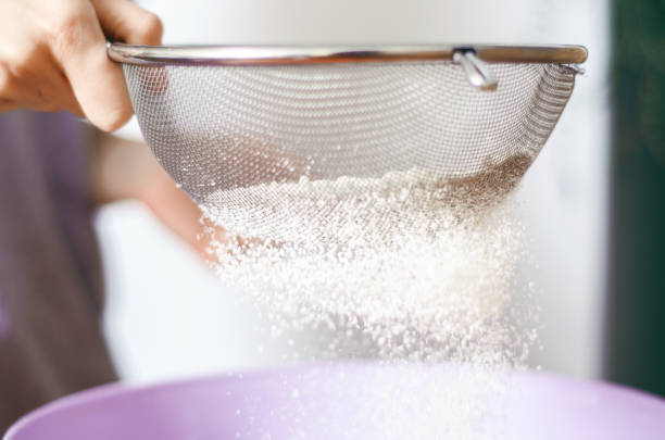 woman flour sifting through a sieve for baking - sifting imagens e fotografias de stock