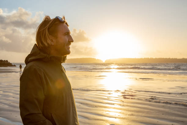 istock Young man standing on beach at sunset watching the waves, wilderness area 1191215856