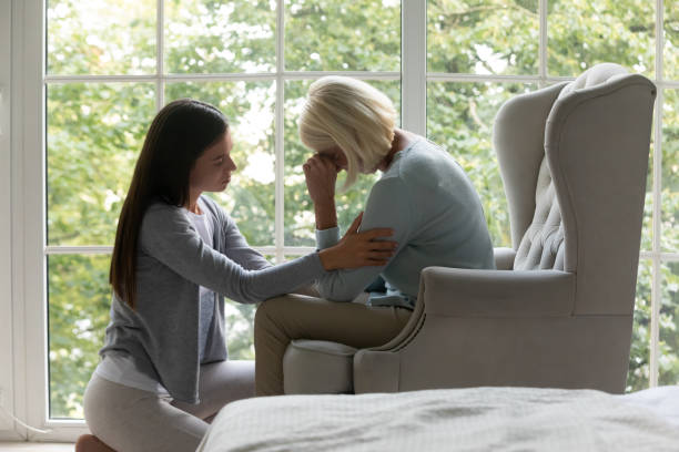 Daughter comforting elderly mother sharing difficult life period giving support Near panoramic window crying elderly mom sit on armchair, near sit her grown up daughter comforting her in difficult life period give support, share pain at divorce, showing attention and care concept widow stock pictures, royalty-free photos & images