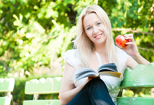 giovane donna lettura libro nel parco - bench sitting tree apple foto e immagini stock