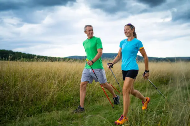 active smiling middle aged couple doing nordic walking sport in grassland with  shallow focus cloudy overcast sky dark clouds front view