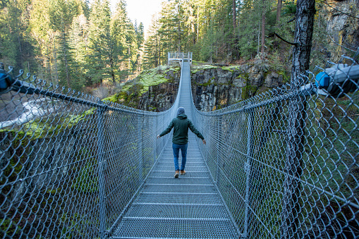 Man walking on suspension bridge crossing canyon in rainforest, river beside, Canada
