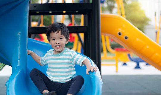 Young asian boy playing on a blue playground slide