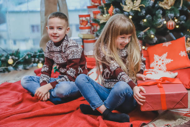 istock Two kids sharing christmas gift boxes sitting in christmas designed atmosphere. 1191242790