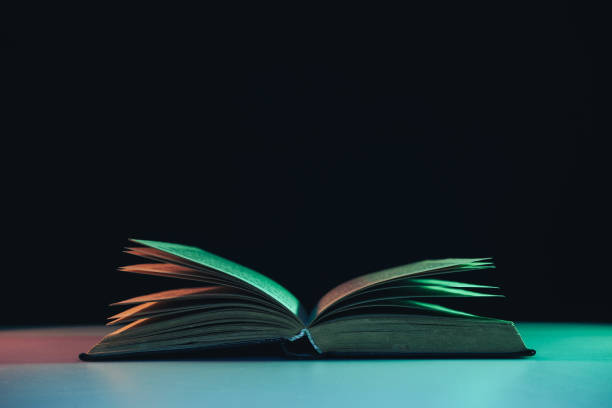 istock Beautiful open old book in the color light on a table and night background. 1191243638