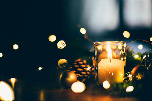 A close-up of a Menorah burning one candle and Shamash to celebrate the first night of Hanukkah sitting on a stained wooden fireplace mantel with a blue Dreidel and gold coins framed mirror hanging on the wall