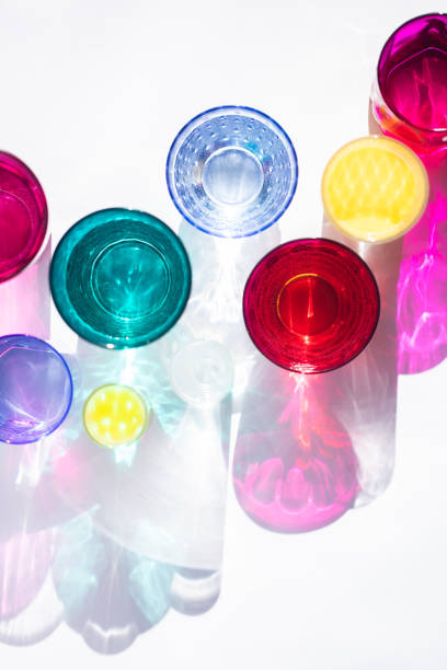 Glass goblets create wonderful coloured shadows on a solar table. The shadow of sunlight reflect to glass of pink and yellow, emerald colors. Top view