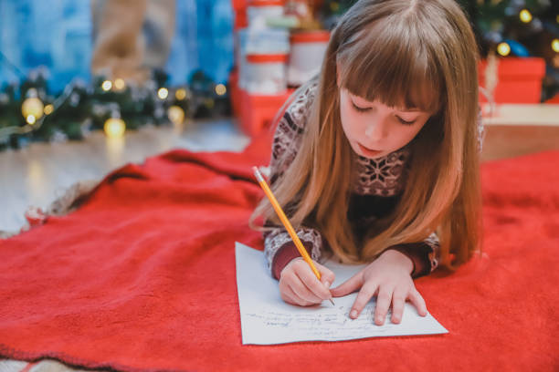 kleines mädchen, sicher, dass sie sich das ganze jahr gut benimmt, schreibt einen brief an den weihnachtsmann, um das geschenk zu bekommen. - child thinking writing little girls stock-fotos und bilder