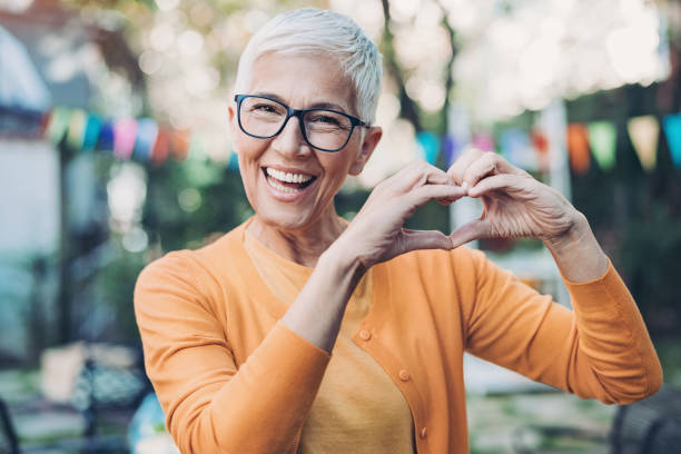 Lovely mature woman making heart shape with hands Portrait of a smiling senior woman gesturing outdoors peace sign gesture photos stock pictures, royalty-free photos & images