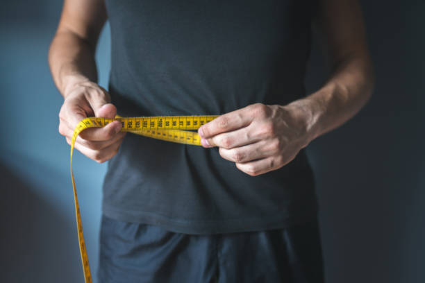 homem magro que mede sua cintura. estilo de vida saudável, emagrecimento corporal, conceito de perda de peso. - body concious - fotografias e filmes do acervo