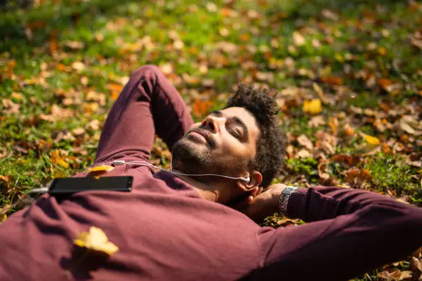 Photo of Relaxed young man laying on ground and listening to music on autumn day.