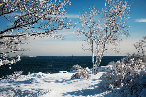 The snow covered rocky coastline at Fort Williams Park and ram island ledge light station in portland Maine on a sunny blue sky day.