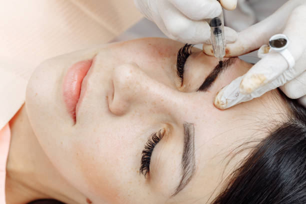 Permanent makeup, tattooing of eyebrows. Cosmetologist applying make up Permanent makeup, tattooing of eyebrows. Cosmetologist in white gloves applying make up with machine for woman in beauty salon durability stock pictures, royalty-free photos & images