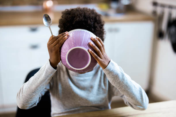 Small black kid eating his breakfast from a bowl at dining table. Little African American boy eating breakfast from a bowl at dining table. black people eating stock pictures, royalty-free photos & images