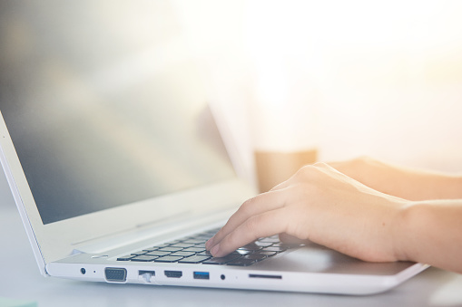 Woman working at lap top with blank screen, female's hands on keyboard of PC, online work, girl having online work, girl typing text, faceless portrait of office worker. Modern technology concept.