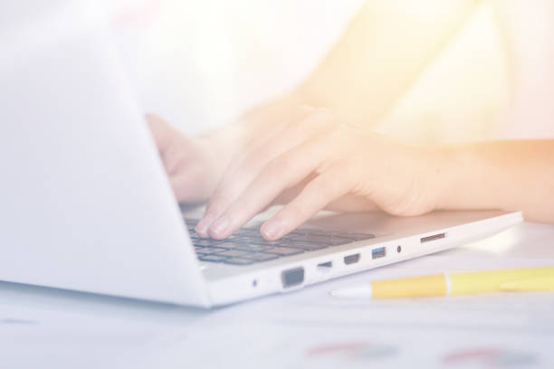 istock Woman's hands typing on keyboard of notebook, sitting at table against white background, white lap top and yellow pen on desk, female working online via Internet, checking her e mail, has message. 1191261273