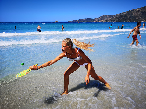 Villasimius, Italy - August 16, 2019: Woman plays beach tennis on the shore of the blue Sardinian sea.