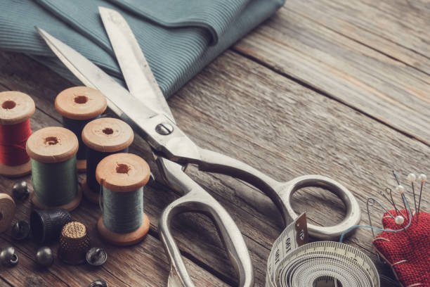 istock Retro sewing items: tailoring scissors, cutting knife, thimble, wooden thread spools, cushion for including pins, fabrics and sewing accessories. 1191261640