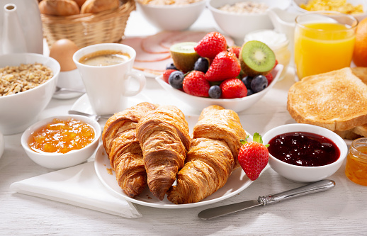Breakfast with croissants, coffee, juice,  jam, cereals and fresh fruits on a wooden table