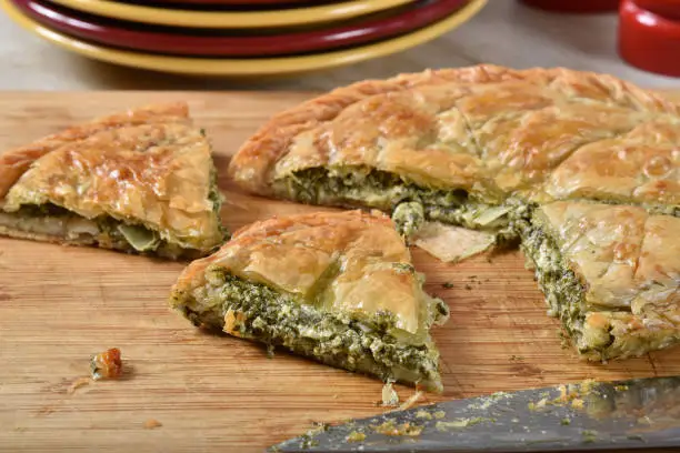 Homemade spanakopita slices on a cutting board by serving plates