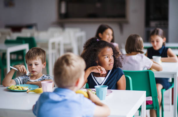 grupa wesołych małych dzieci w stołówce, jedząc obiad. - cafeteria zdjęcia i obrazy z banku zdjęć