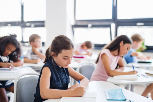 petits écoliers concentrés s'asseyant au bureau dans la salle de classe, écrivant. - schoolgirl little girls crayon human face photos et images de collection