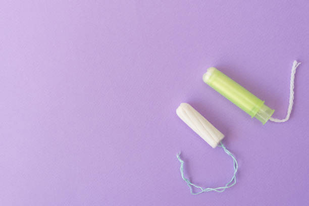 dos tampones de algodón con aplicador verde claro y sin aplicador sobre fondo violáceo. tipos higiénicos de tampones. menstruación, protección, concepto de comparación, plano, espacio de copia, vista superior - tampon menstruation applicator hygiene fotografías e imágenes de stock