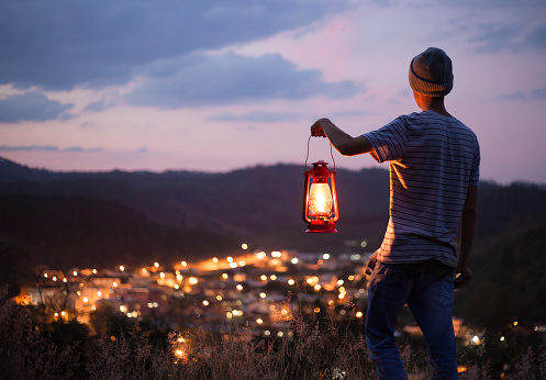 young man camping with a kerosene lantern lit to illuminate