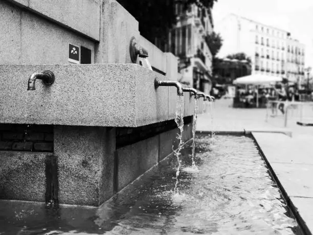 Public drinking water fountain in Madrid, Spain. Perspective view of faucets pouring water in Black and White.