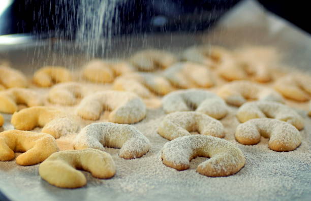 sprinkling powdered sugar on a baking sheet with vanilla crescents (vanillekipferl) - baking traditional culture studio shot horizontal imagens e fotografias de stock