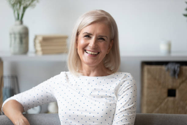 istock Headshot aged woman smiling sitting on couch looking at camera 1191287522
